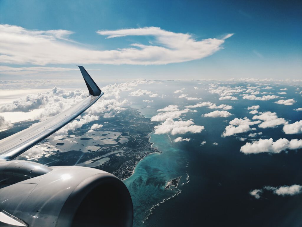 View from airplane window showing the wing engine and turquoise ocean below with clouds — representing travel reward point redemptions for flights.